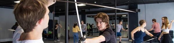 Theatre students in a mirrored studio practicing fencing.